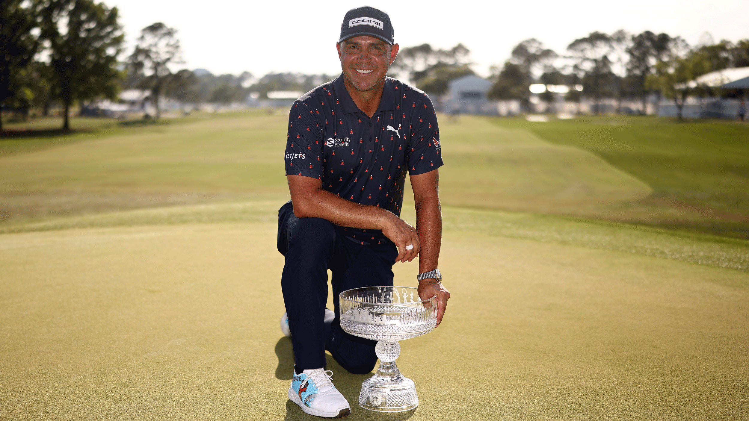 Gary Woodland kneels down beside the Texas Children's Houston Open trophy on the 18th green at Memorial Park