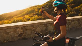 Woman stopping on the side of a road on her bike to take pictures with phone at sunset