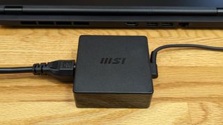 The MSI Modern 14 H power brick sitting behind the laptop as a size comparison