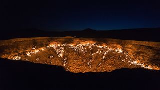 A picture of the Darvaza gas crater at night shows fire burning inside the crater.