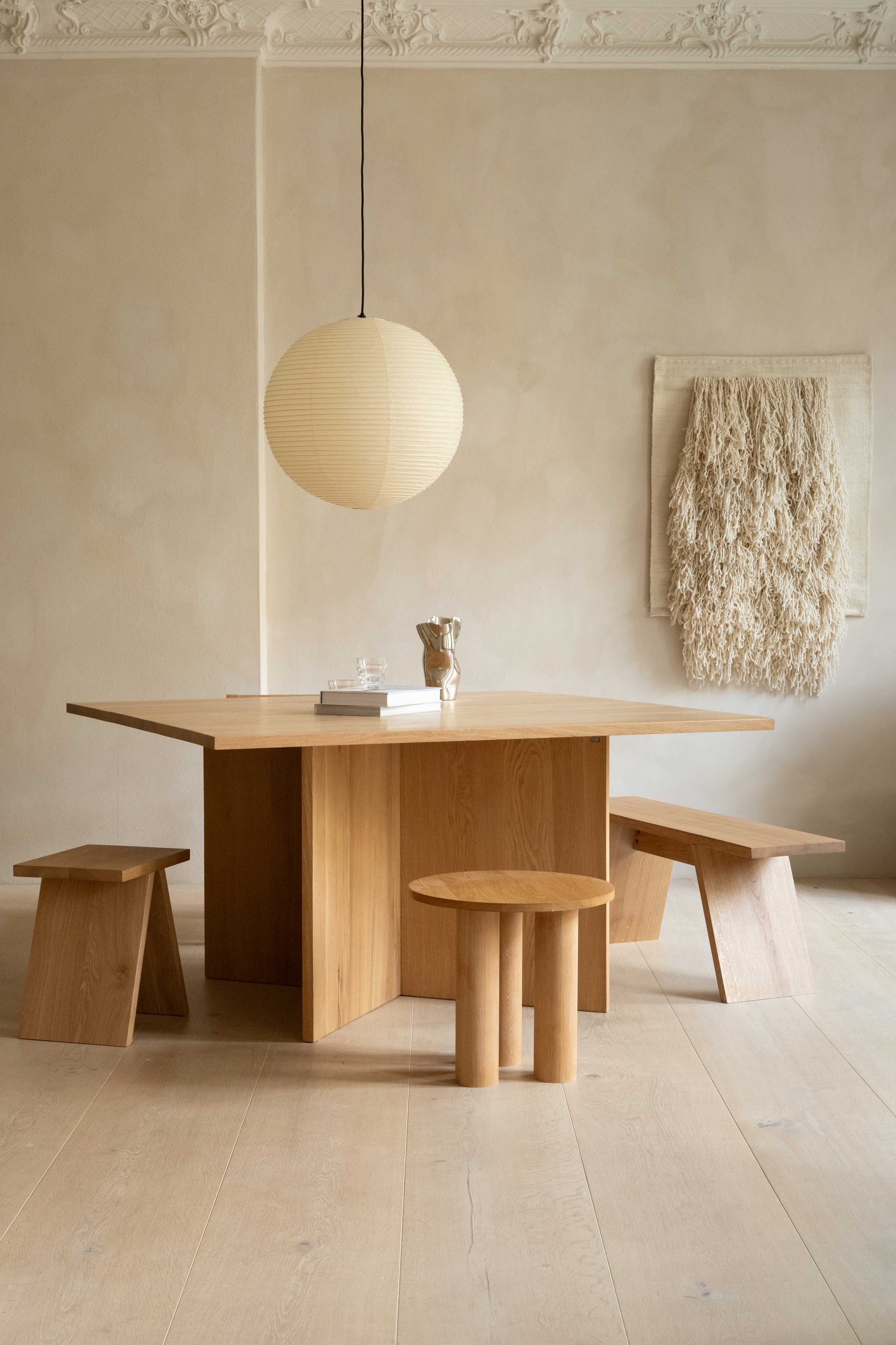 modern dining room with limewash walls, ornate molding, wall hanging, pendant light hanging over a square timber table with timber stools