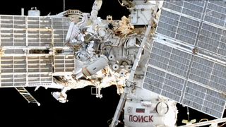 an exterior view of a space station includes two spacesuited cosmonauts at work during a spacewalk