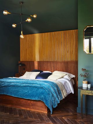 bedroom with dark green walls and wood paneling bedhead and wooden floor with blue bedcover