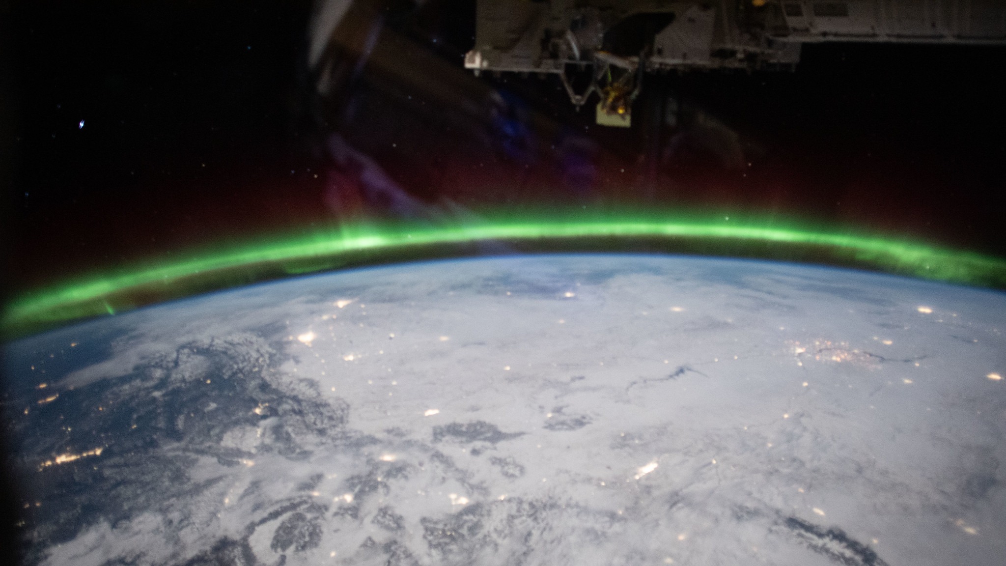 white snowy land of earth visible from space. an aurora is around the edges of our planet