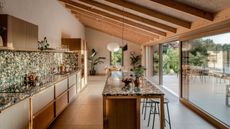 a narrow kitchen layout with a central island unit and sloping roof with a wall of sliding glass doors out to the garden