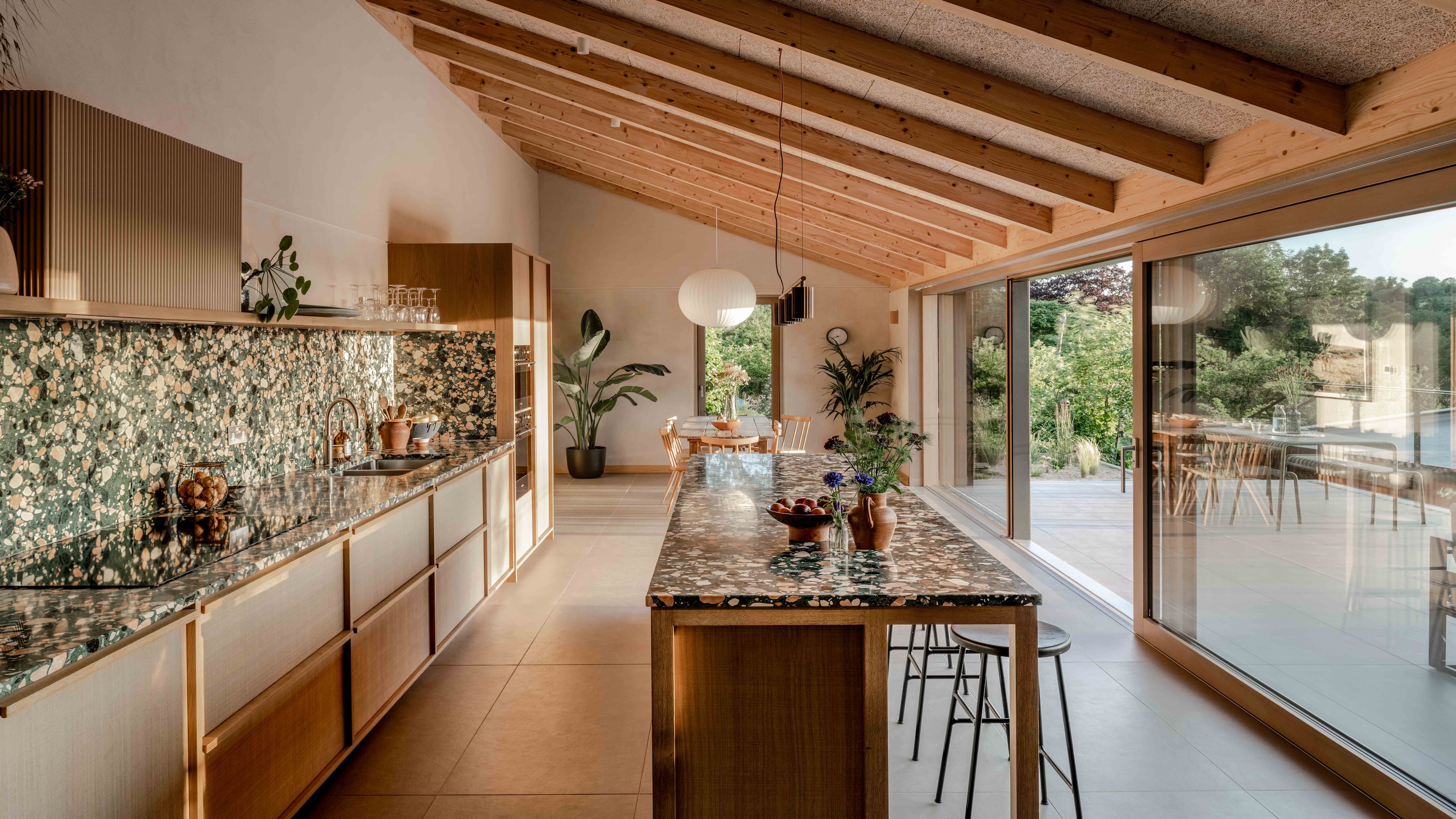 a narrow kitchen layout with a central island unit and sloping roof with a wall of sliding glass doors out to the garden