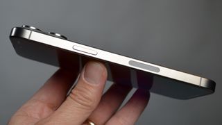 Apple iPhone 15 Pro Max sivuttain ihmisen kädessä harmaata taustaa vasten