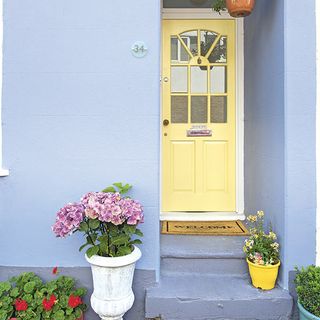 blue house exterior with yellow door and flower pots