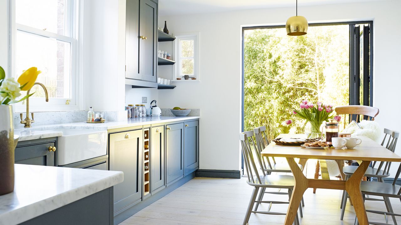 small kitchen with dark blue cabinets, wood dining table and brass light fixtures