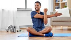 Man sitting on a yoga mat in his living room performing a stretching exercise and smiling