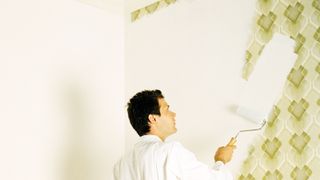 Man painting over patterned wallpaper with roller