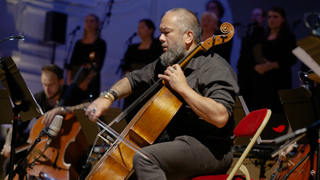 Olivier Derivière and Eric-Maria Couturier and a chamber orchestra perform music from A Plague Tale: Requiem alongside the Estonian Philharmonic Chamber Choir. The foreground of the image is the first chair Cello player.