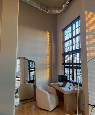 A gray room with a mirror and desk next to a window with black blinds