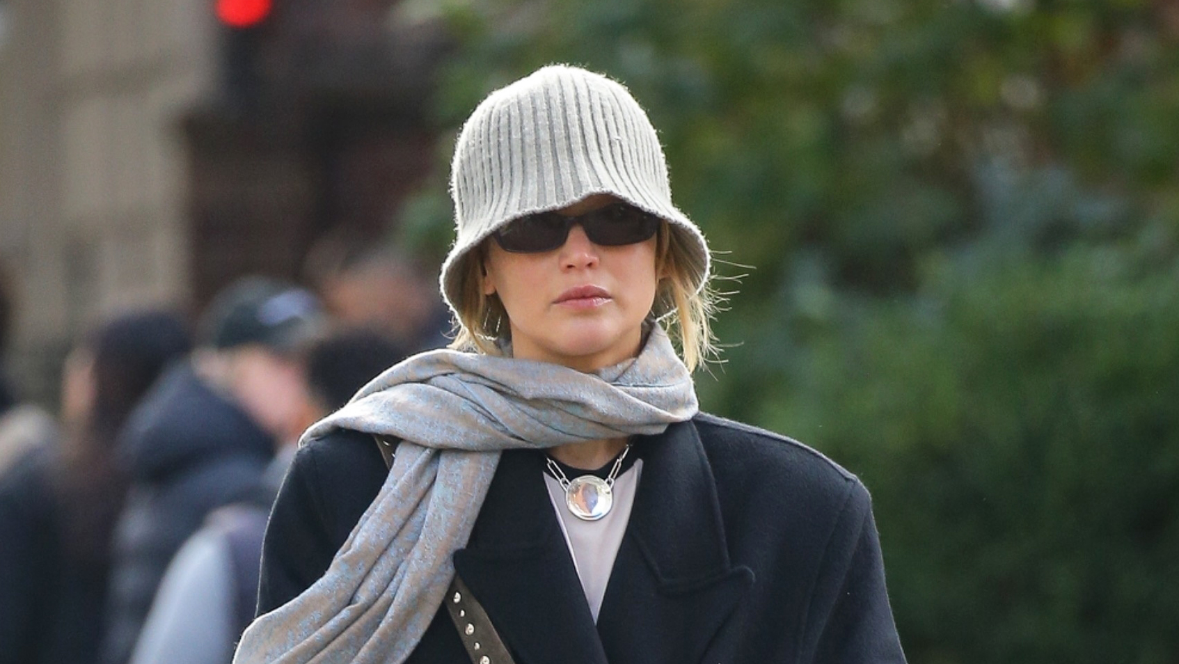 Jennifer Lawrence wearing a knit beanie, oversized coat, scarf, flats, and suede studded bag in NYC