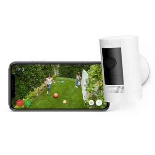 White Ring Outdoor Camera Battery with black lens next to a smartphone 