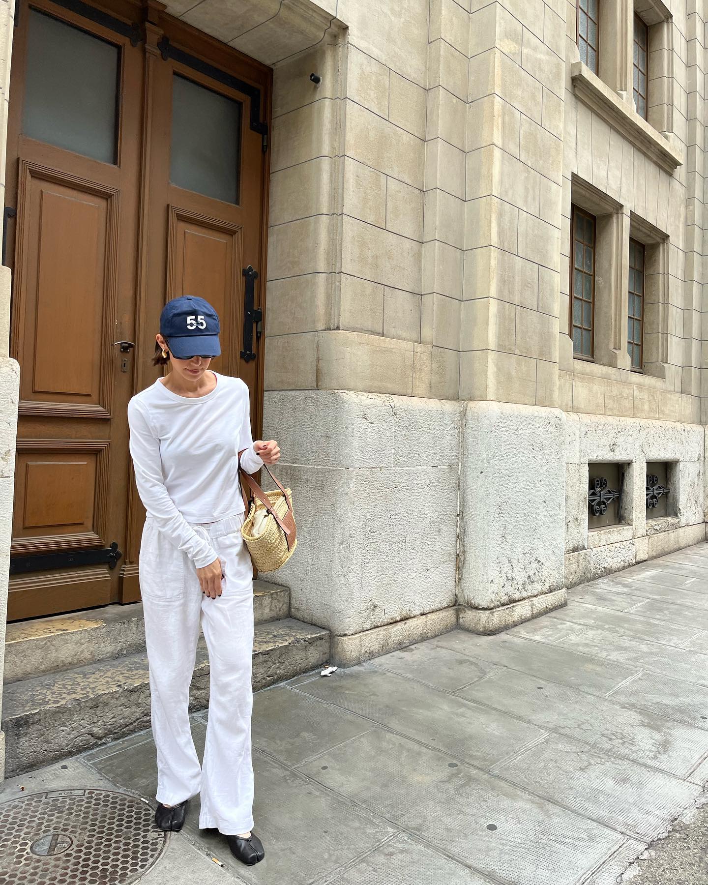 Alaina Imperio wearing a blue baseball cap, long-sleeve white T-shirt, and white linen pants.