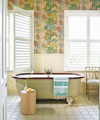 Bathroom inspired by nature, with wood rim bath, metro wall tiles and two windows with shutters, bamboo chair, log-style stool and feature wallpaper