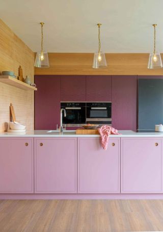 A pastel pink kitchen with purple walls and trio of overhead pendant light fixtures