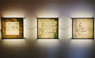 White textured wall, in a three square wall art pieces of satellite imagery, back lights behind images