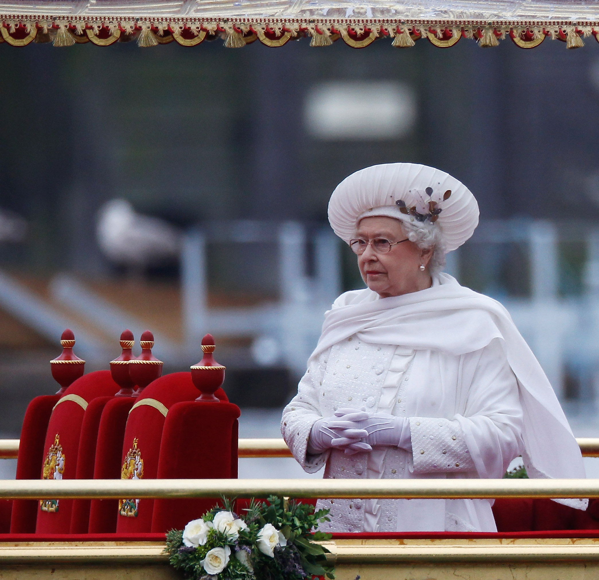 Queen Elizabeth on a boat in a white coat, scarf and hat
