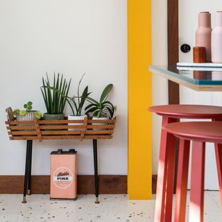 White painted kitchen with bright yellow pillar, wooden houseplant holder, and pink stools