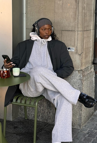 what to wear in 30-degree temperatures, shown in a photo of a woman sitting outside at a cafe wearing an oversize gray blazer over a white hoodie layered under a fleece sweatshirt with matching gray sweatpants and black tabi loafers