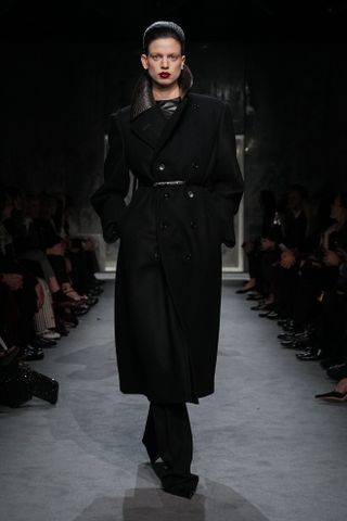 A model wearing a black tailored coat walking in Haider Ackermann's first Tom Ford runway show during Paris Fashion Week.