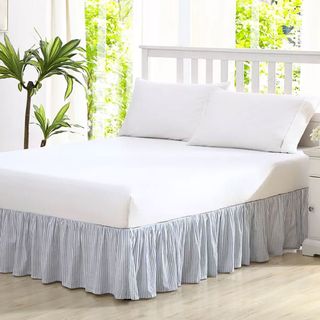 blue and white stripe bedskirt on bed with white wooden headboard in bedroom with plants