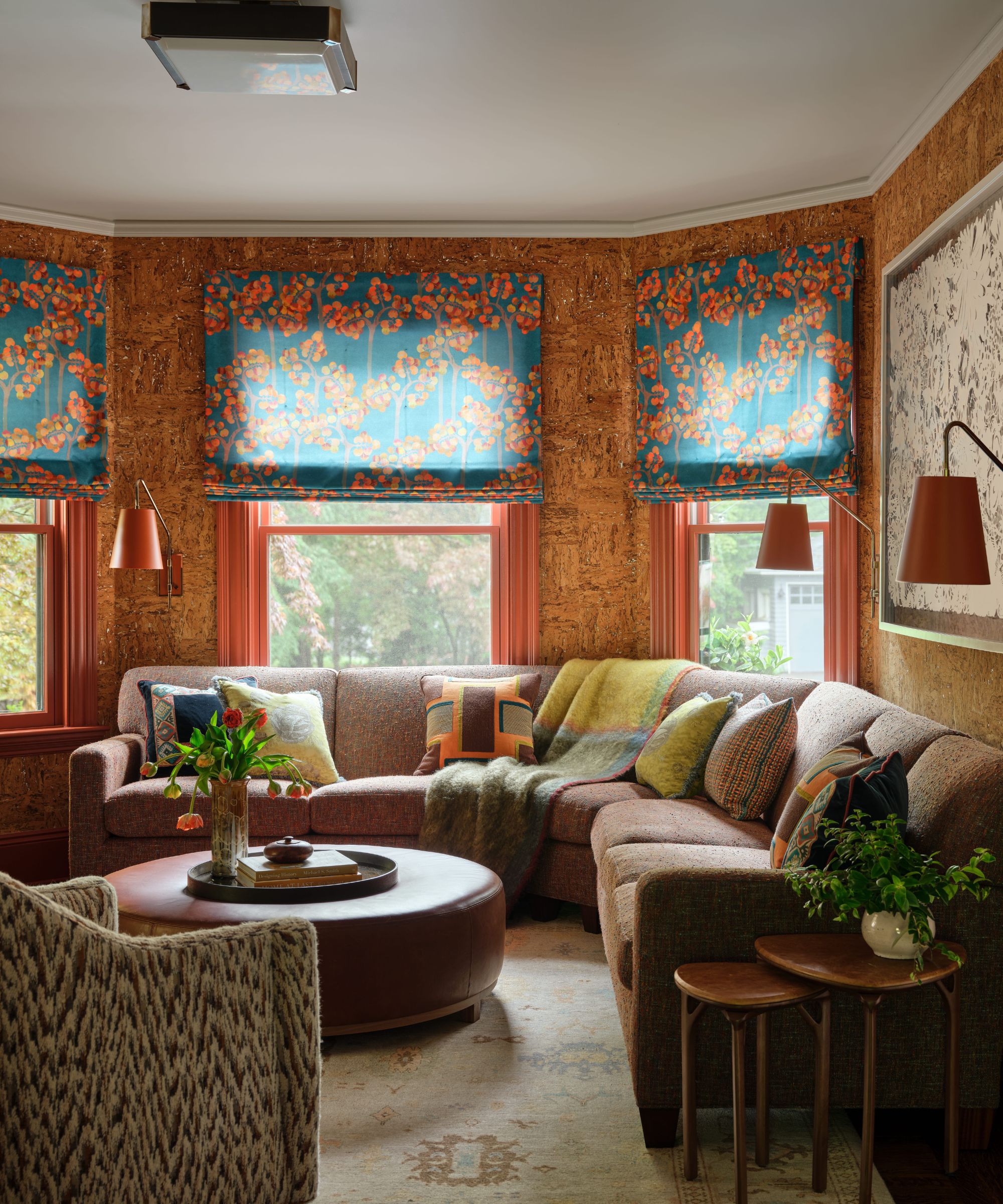 Cozy living room with cork walls, a brown sectional sofa, and vibrant teal and orange floral Roman window shades.