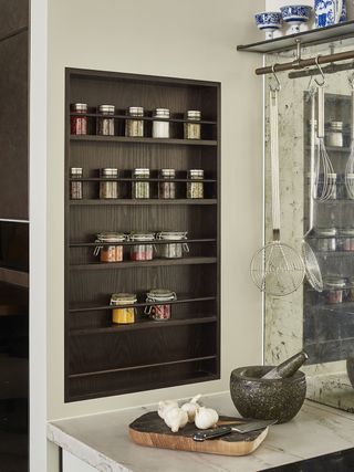 kitchen with spice rack storage, inset into wall with dark brown wood, mirrored splashback and hanging utensils