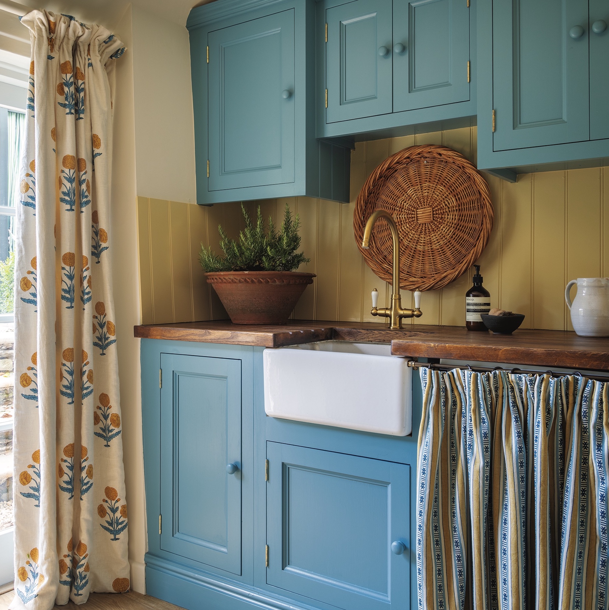kitchen with blue painted cabinets, butler sink with brass tap and curtains