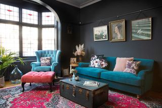 Black living room with blue velvet sofa, set of three pictures, pink ottoman and red traditional rug