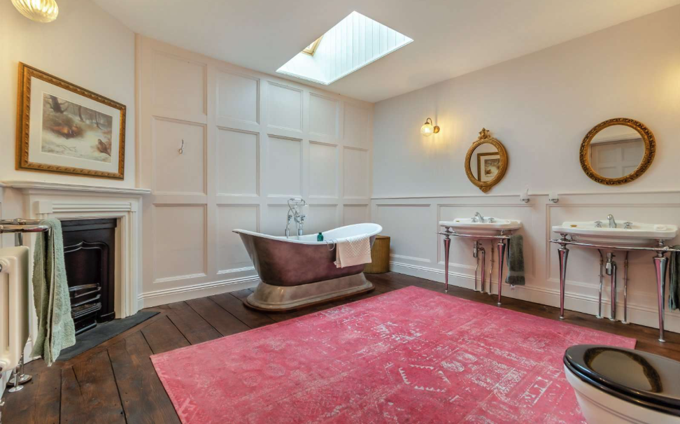 A freestanding brass bath in the centre of a wooden-floored bathroom