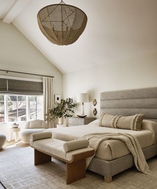 coastal meets scandi style bedroom with a grey upholstered bed, a boucle armchair and a large seagrass woven ceiling light