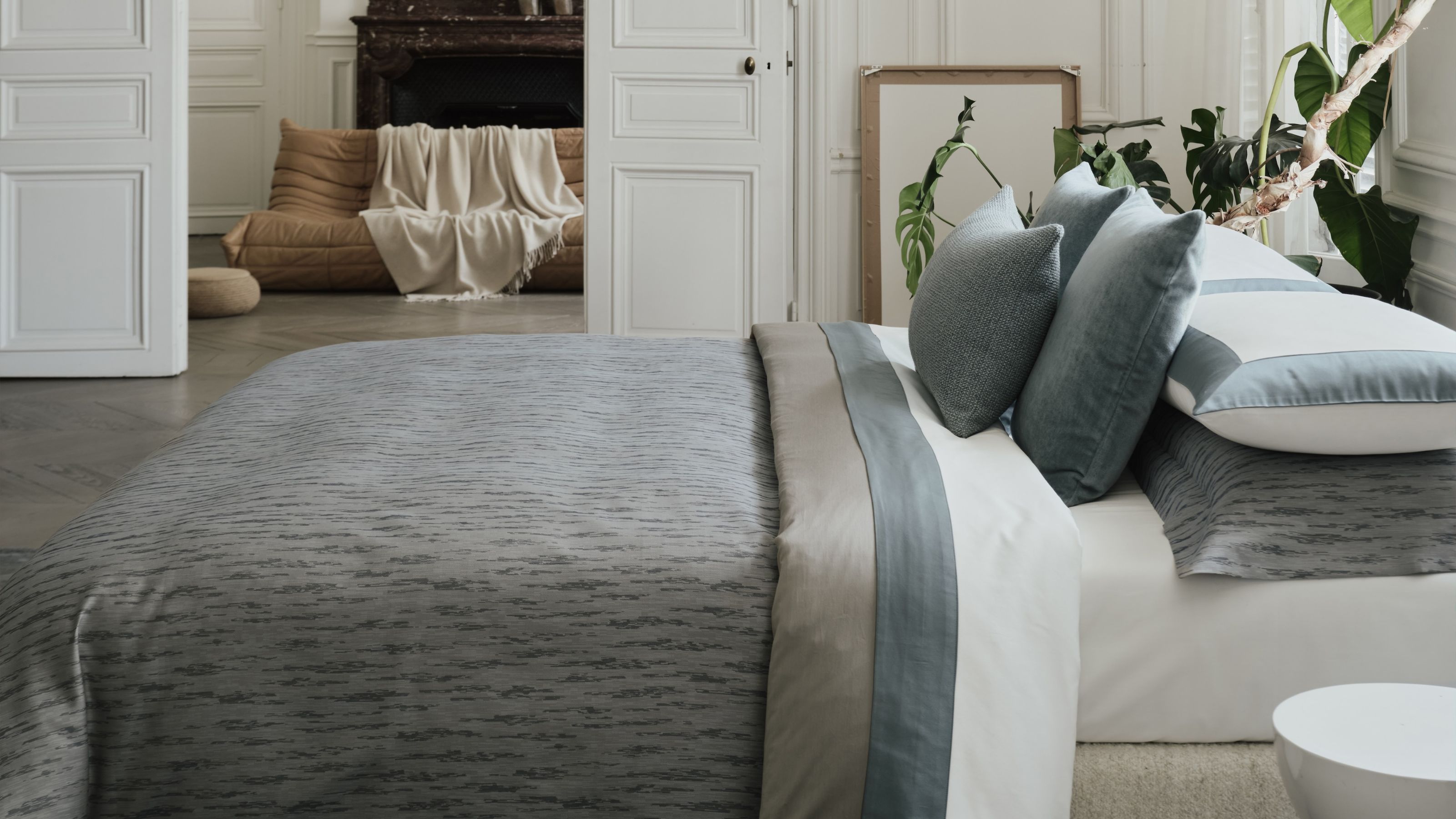 Image of a luxurious bed that has white sheets and stone blue and gray bedding. 