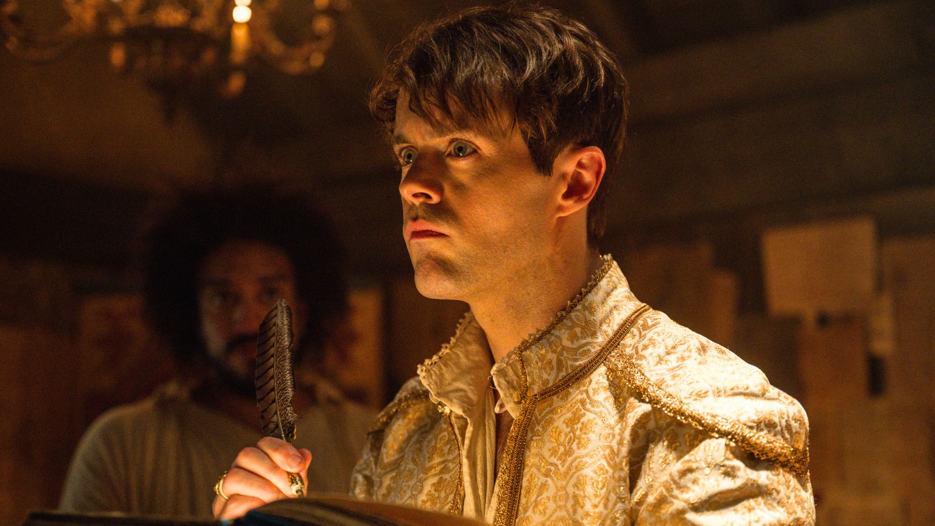 Jaskier holds a quill and paper