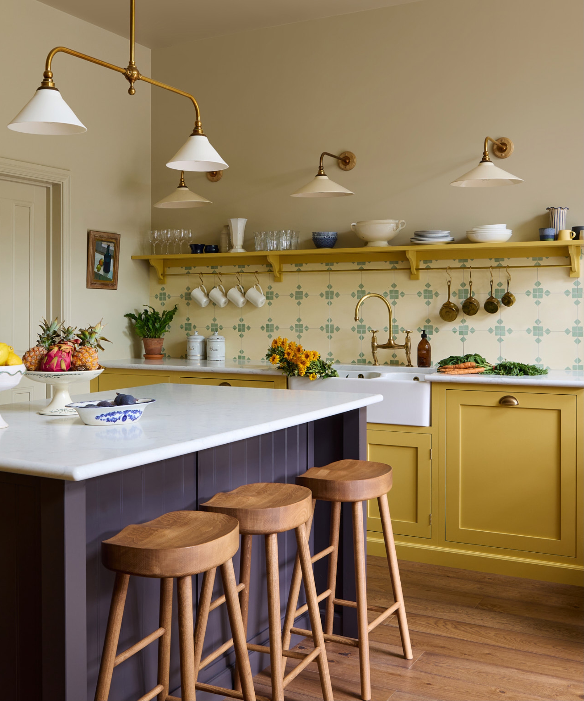 An open plan kitchen with yellow cabinets, and aubergine island, and cream and light green patterned wall tiles