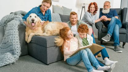 A big family and their dog sit around their living room smiling and laughing.