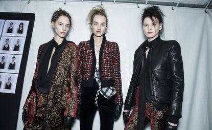 Three women, one wearing a black and gold trouser suit, one in a black and red jacket and black corduroy trousers, and one in a black leather jacket