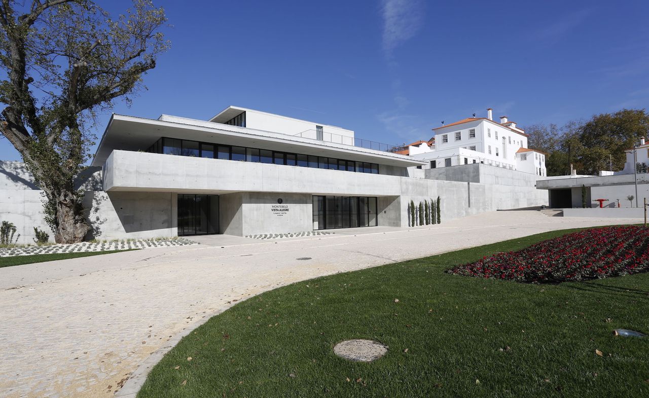 Exterior view of the Montebelo Vista Alegre hotel. Modern-looking concrete building with a wide driveway, and a lawn with red flowers in the middle.