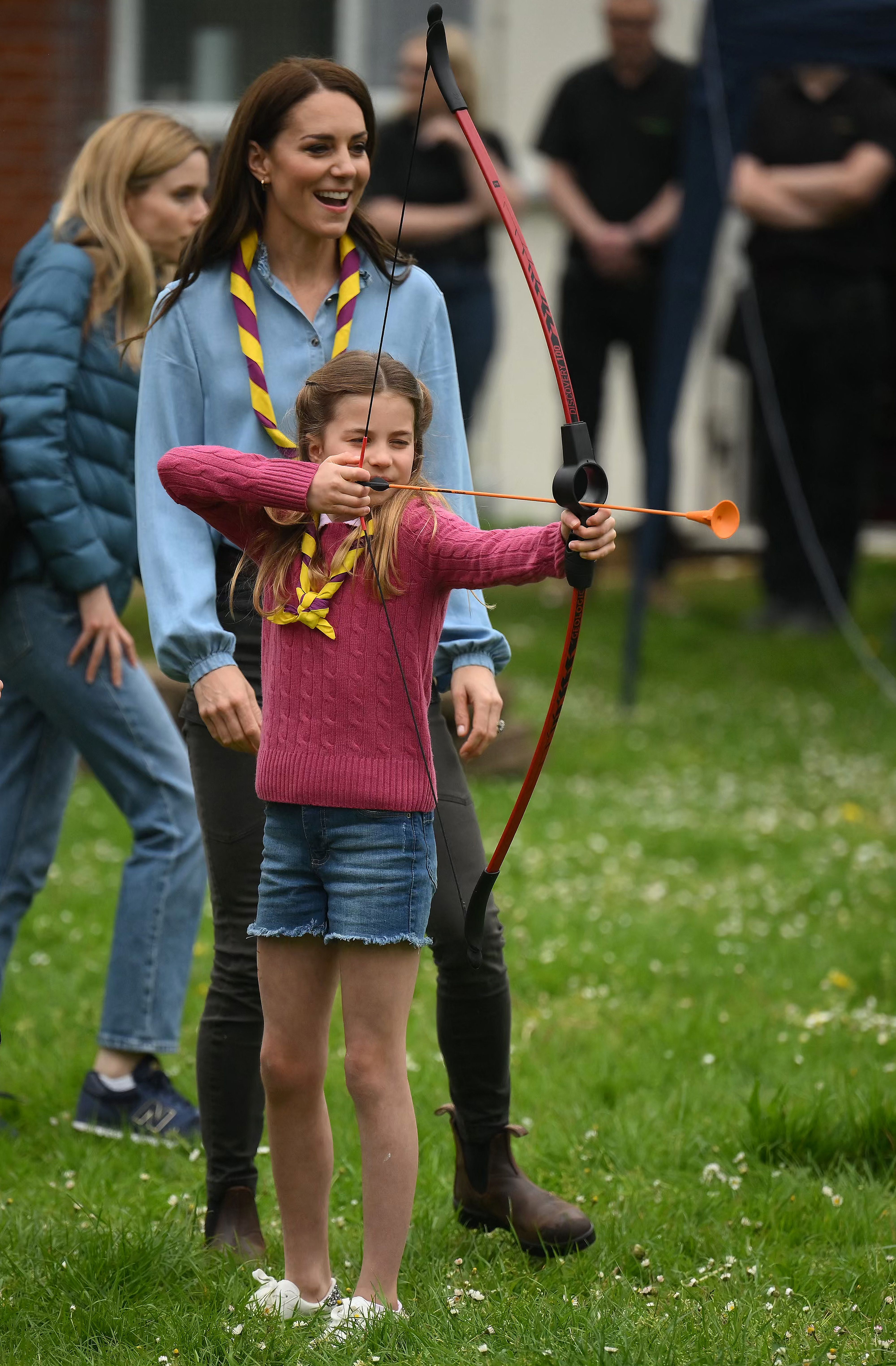 Princess Charlotte doing archery while Princess Kate watches behind her and smiles