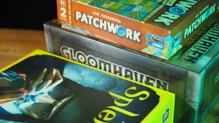 Splendor, Patchwork, and Gloomhaven: Jaws of the Lion boxes stacked on a wooden table