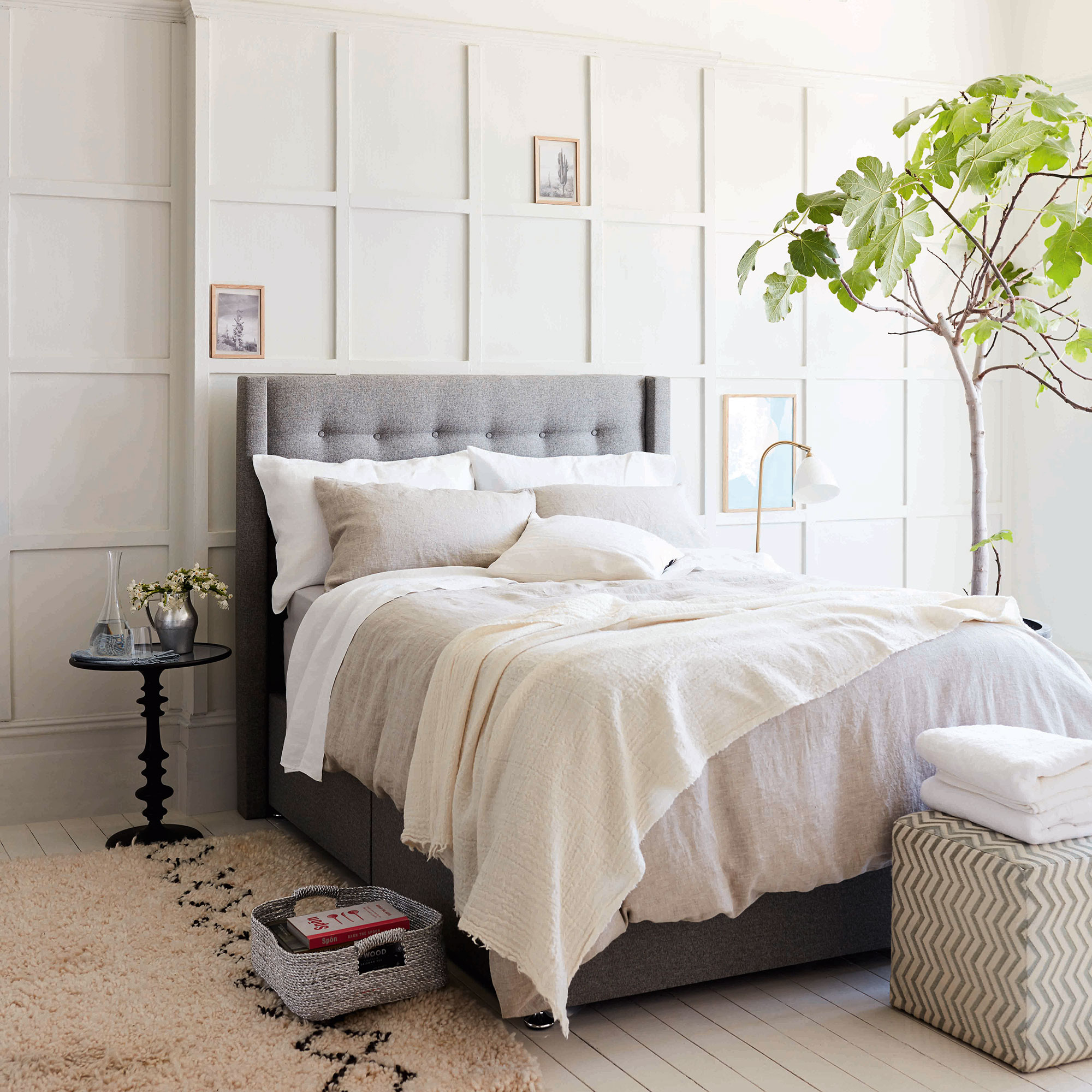 White bedroom with panelling on wall and large grey double bed and fig tree next to it