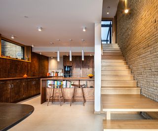 inside of eco house with stone wall timber staircase and dark wooden kitchen