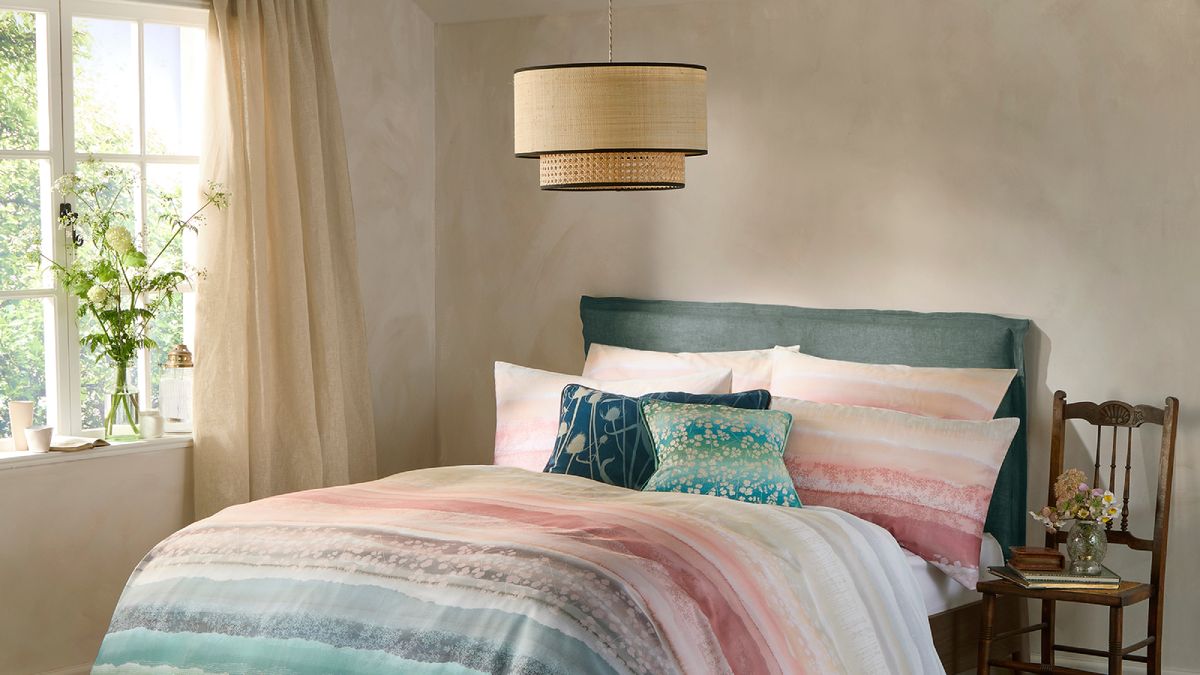 bedroom with pink and blue striped bedding, light walls, wicker ceiling pendant and chair by side of bed