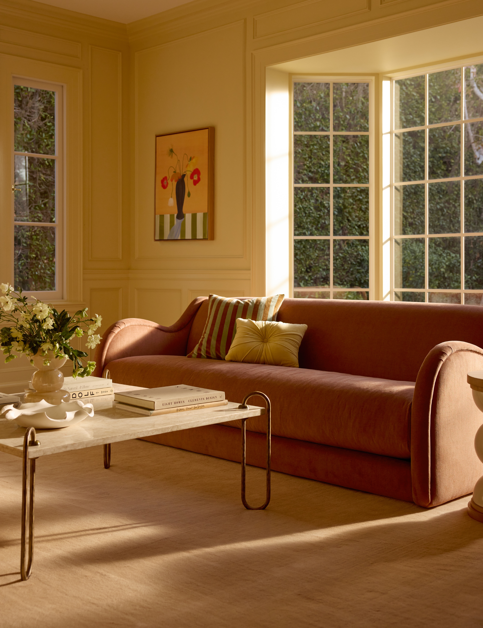 Pastel yellow living room featuring a low-slung sofa, sculptural coffee table, and modern art.