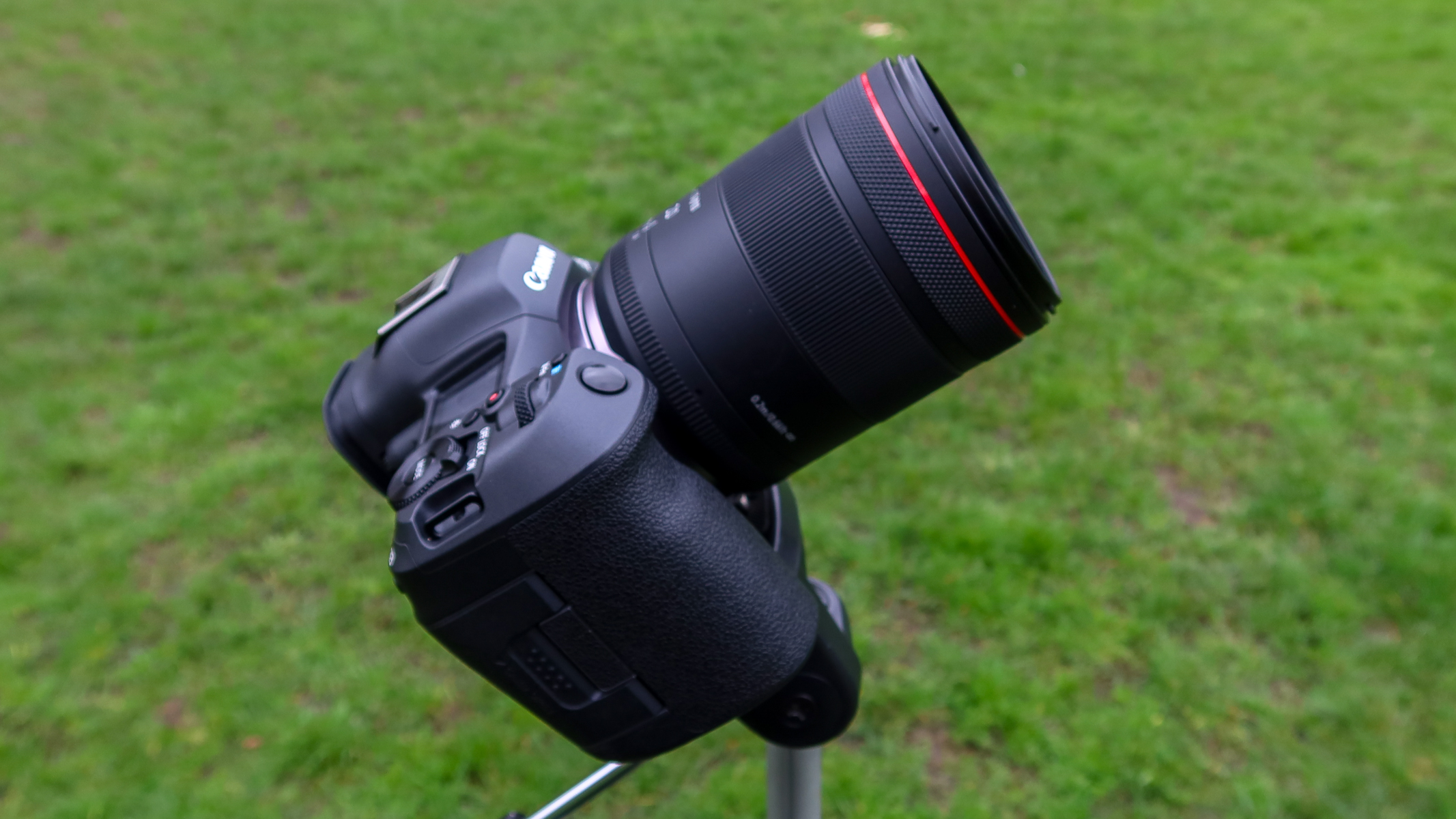 A side view of the Canon RF 20mm f/1.4 L VCM lens attached to the Canon EOS R5 II with grass in the background.