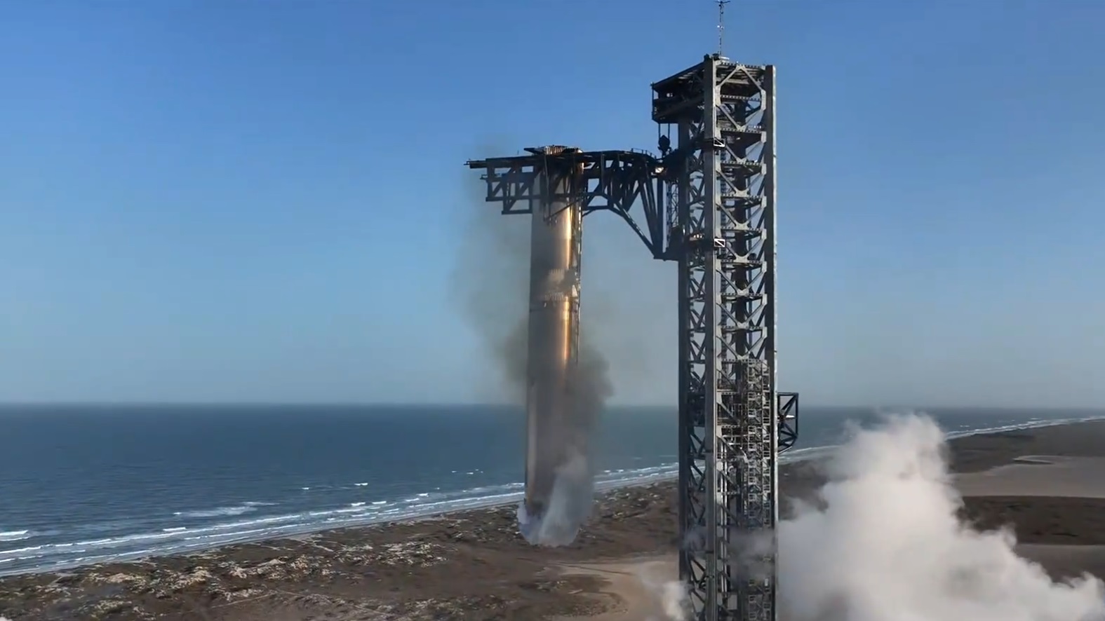 A giant silver SpaceX rocket Booster hangs between giant metal arms after landing at its launch pad on March 6, 2025.