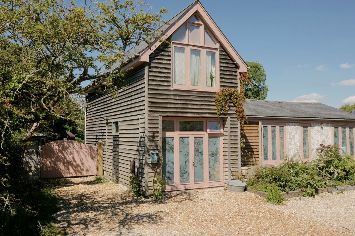 A house with pink exterior around the windows and wooden gate with timber structure