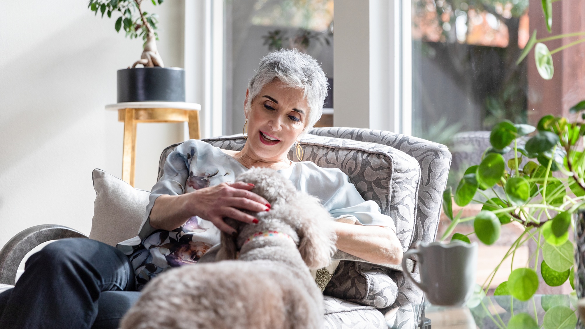 An older woman pets her dog at home.